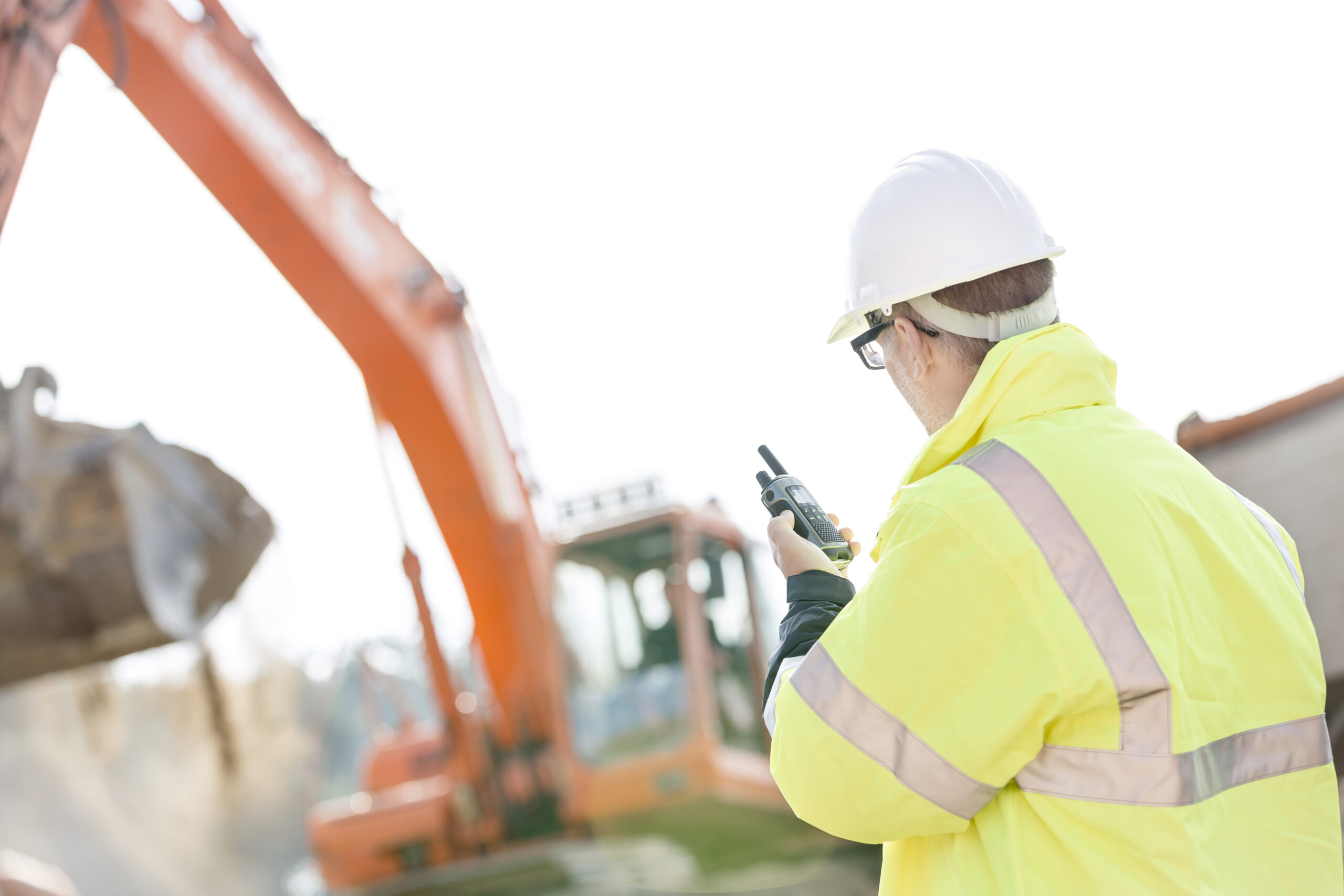 Baustelle, Mann mit Funkgerät vor einem Baggger