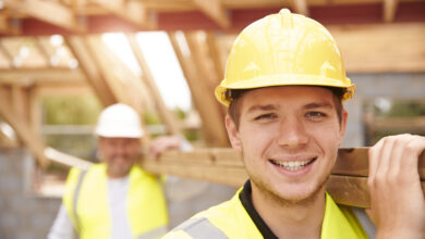 Builder And Apprentice Carrying Wood On Construction Site