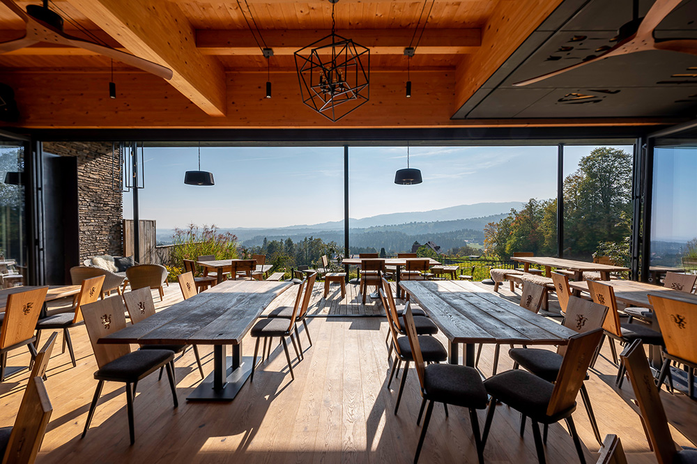 © allinone creative OG für Solarlux GmbH Gastraum mit Holzmöbel mit Blick auf grüne Landschaft