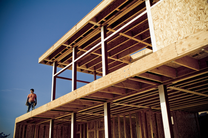 Ein Mann steht auf einem Holzbau und blickt hinunter.