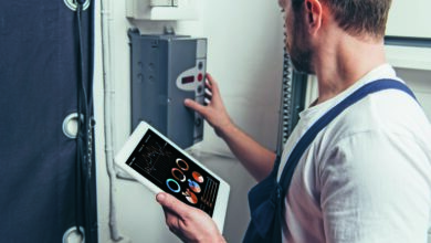 male electrician holding digital tablet with graphs on screen and checking electric box.