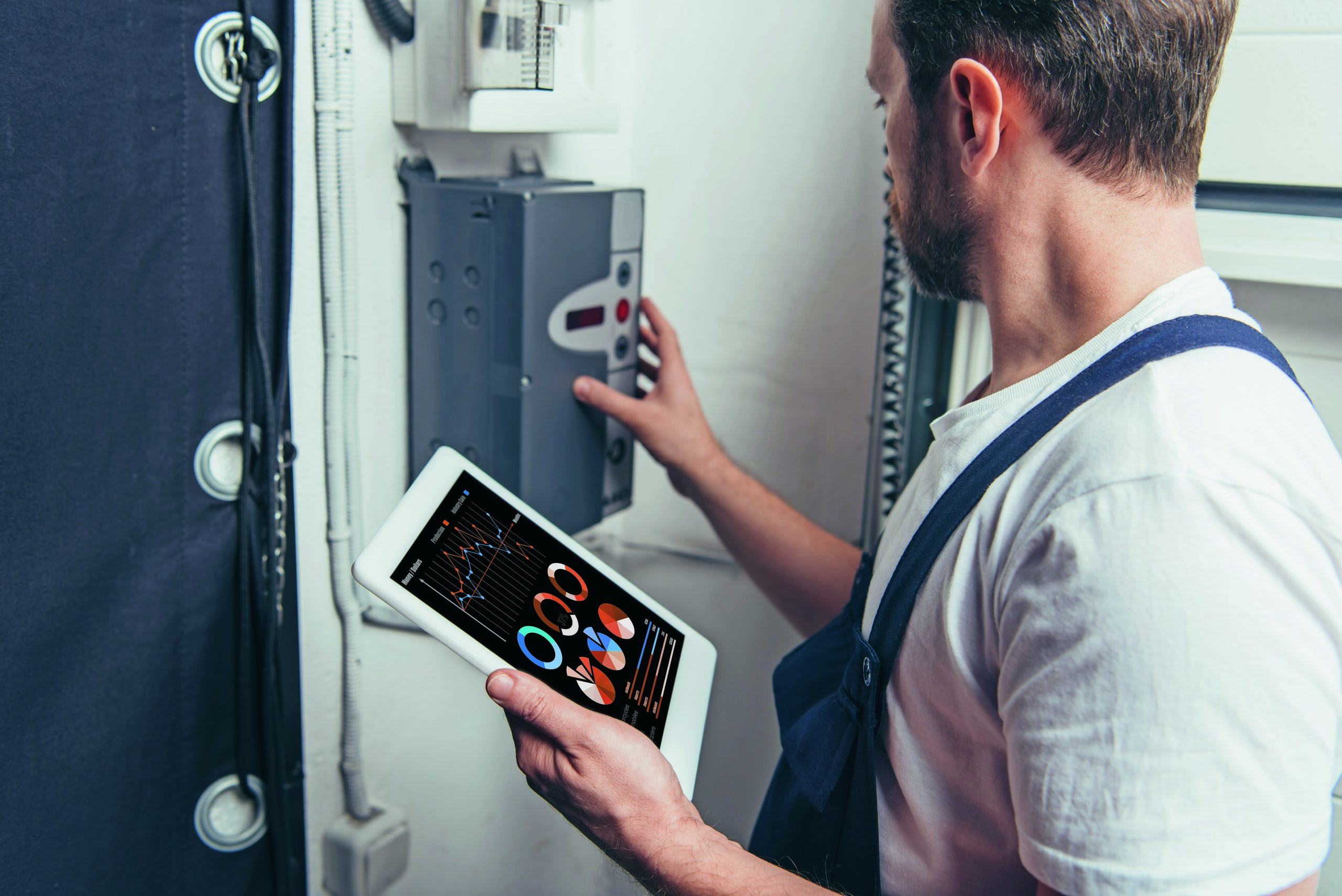 male electrician holding digital tablet with graphs on screen and checking electric box.