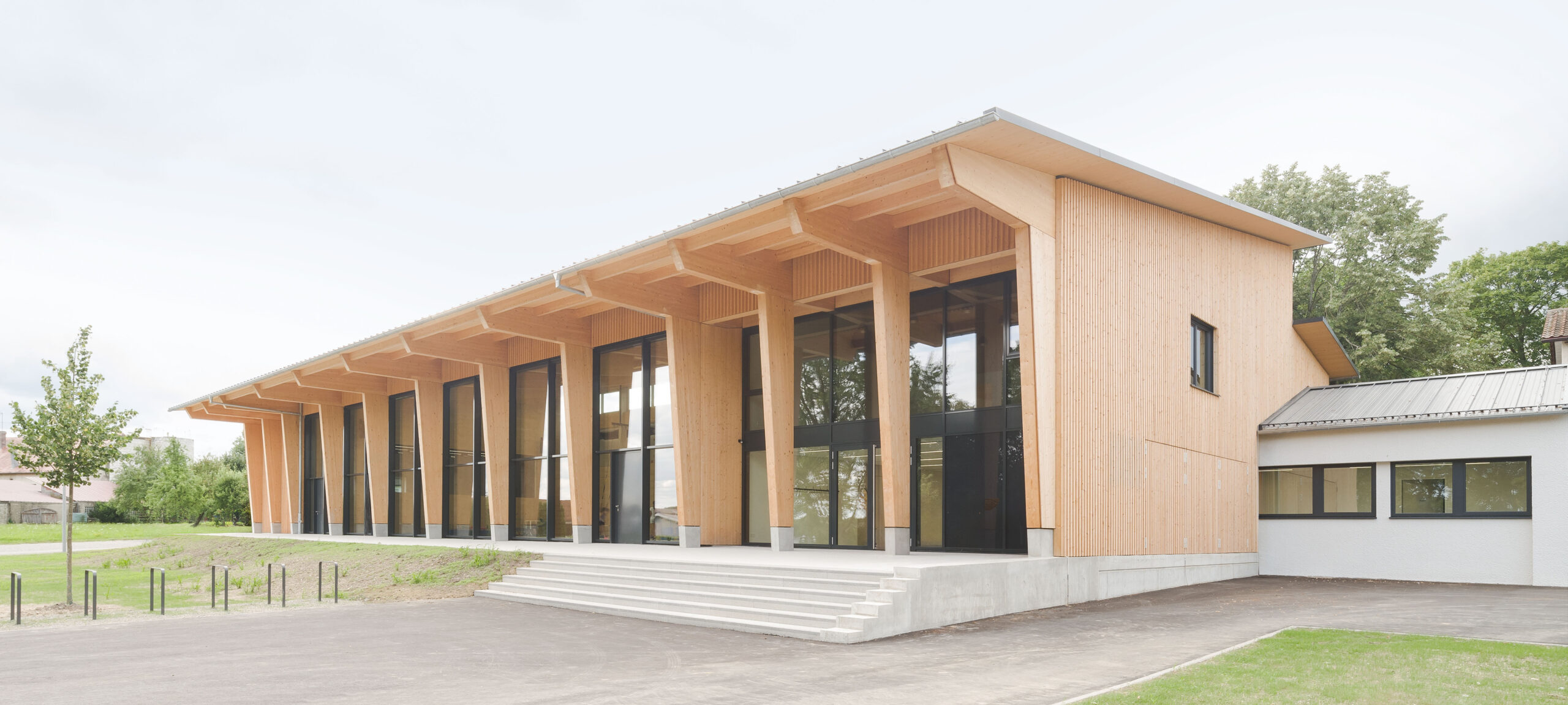 Die heutige Mehrzweckhalle im deutschen Ingerkingen zeigt, welche Ästhetik eine behutsame Sanierung und Erweiterung im Vergleich zu einem Neubau erreichen kann. Die große Dach-auskragung vor der Südfassade schützt die Stützen vor der Glasfassade weitgehend vor Witterungseinflüssen und sorgt gleichzeitig für eine wettergeschützte Terrasse. © Brigida González