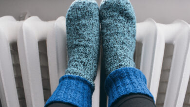 cast iron heating radiators, knitted socks with radiators, women's feet a girl in warm knitted woolen socks near a home heater in the cold winter season. Body part, selective focus. A woman warms her hand in mittens near the heating radiator at home, close-up light knitted socks lie on the radiator during the heating season young girl is warm knitted woolen socks near a home heater in cold winter time. Wool socks close-up on cast iron radiators