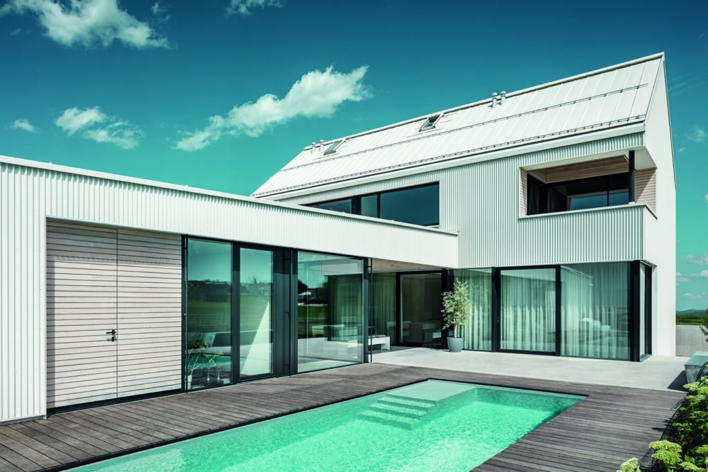 Zwei Gebäudekörper – eines mit Flachdach, eines mit Steildach – fügen sich L-förmig aneinander und komponieren einen geschützten Innenhof mit überdachter Terrasse. © Prefa / Croce & Wir