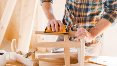 Close-up of young male carpenter sanding wooden chair in his workshop
