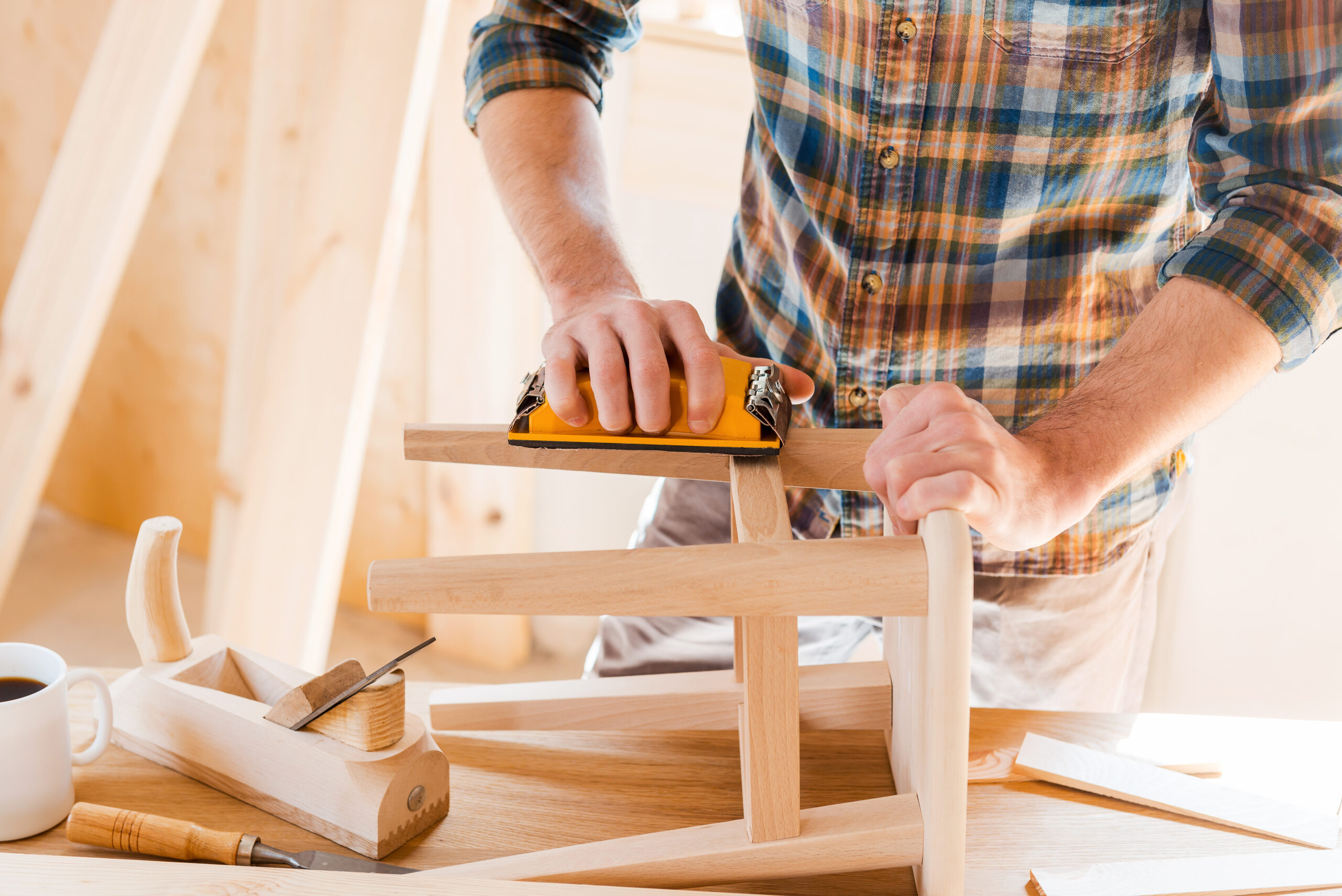 Close-up of young male carpenter sanding wooden chair in his workshop