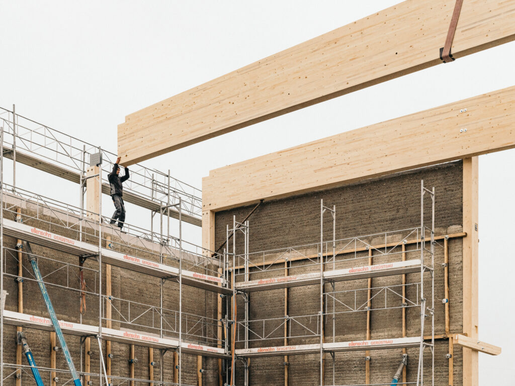 Der Aufbau des Dachtragwerks mit Brettschichtholz-Bindern auf der Stampflehmwand zeigt den neuartigen Hybridbau in Reinform.