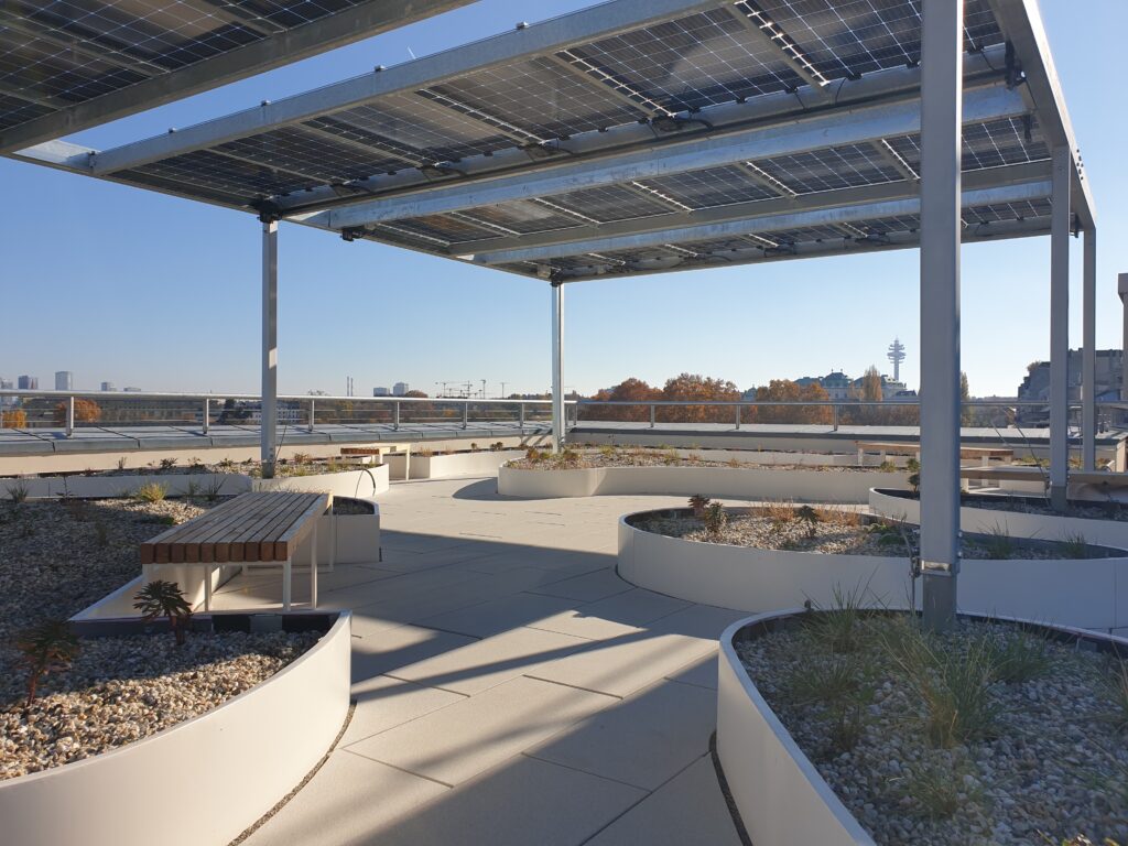 PV-Pergola auf der Dachterrasse: Die Stahlkonstruktion übernimmt Verschattung und Energiegewinnung zugleich – darunter entstehen intensiv begrünte Aufenthaltsbereiche mit Retentionsaufbau.