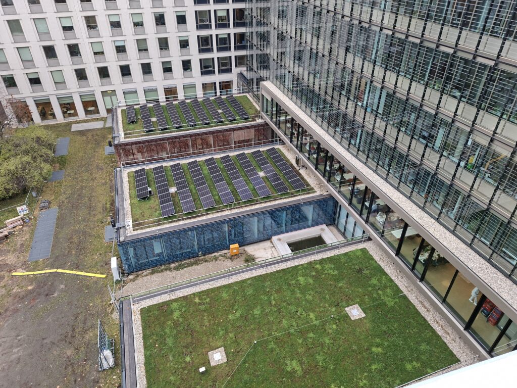 Retentions-Gründächer mit integrierter Photovoltaik im Innenhof: Die extensive Begrünung kühlt die Module, erhöht deren Ertrag und reduziert gleichzeitig Regenabflussspitzen. 