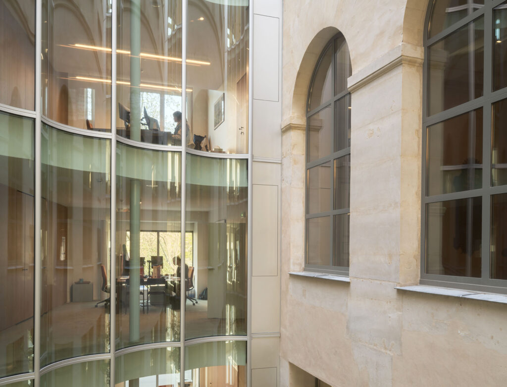 Hinter der gebogenen Glasfassade sind helle, offene Arbeitsbereiche entstanden, die sich zum historischen Innenhof öffnen.