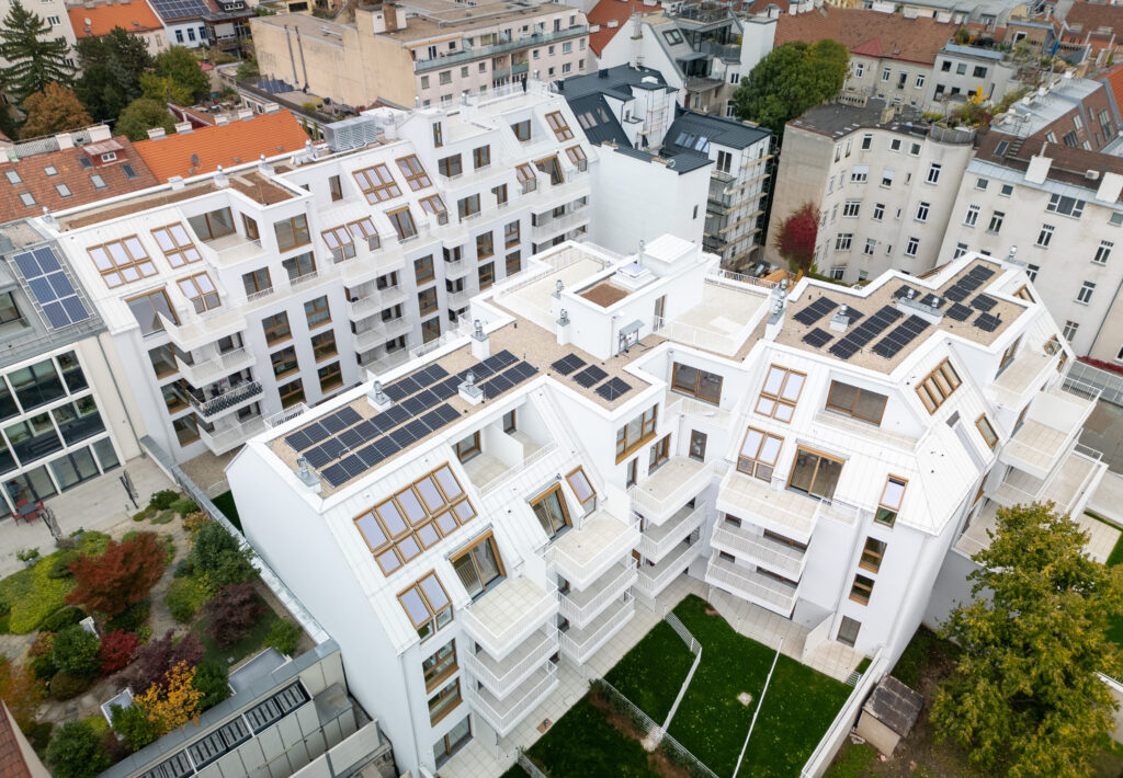 Die Luftaufnahme zeigt das Zusammenspiel von Architektur, Dachfenstern und Photovoltaik. Das Wohnbauprojekt „The Temptation“ verbindet energieeffiziente Gebäudetechnik mit hoher Aufenthaltsqualität.