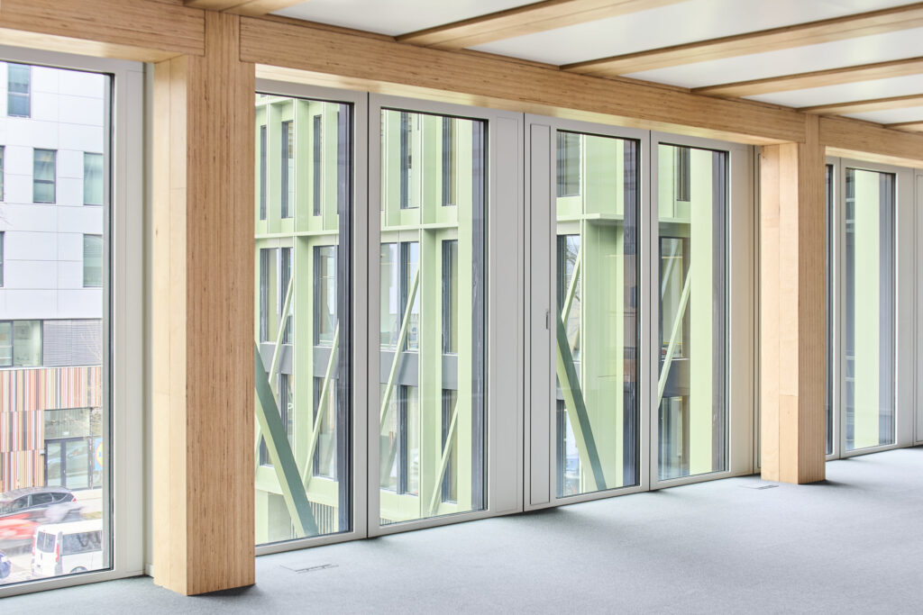 Alle tragenden Holzbauteile wie Stützen, Haupt- bzw- Fassadenträger sind aus Baubuche gefertigt. Bei den Knotenpunkten an den Fassadenseiten schließen die Fassadenträger beidseitig an die Stützen (b x h: 36 cm x 40 cm) an, wo sie auf 10 cm tiefen Ausklinkungen lagern.