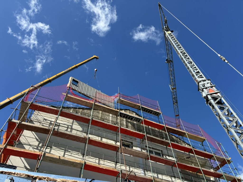 tigte Fassadenmodule werden auf der Baustelle angeliefert und mit dem Kran am Bestandsgebäude montiert. 